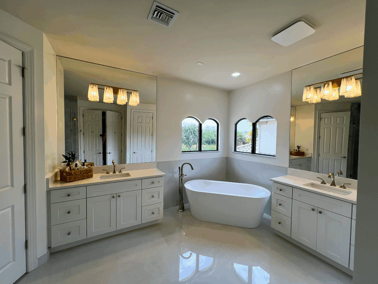 Luxury master bathroom remodel by Nakamura Contractors — freestanding tub, dual white vanities, and arched windows in South Florida.