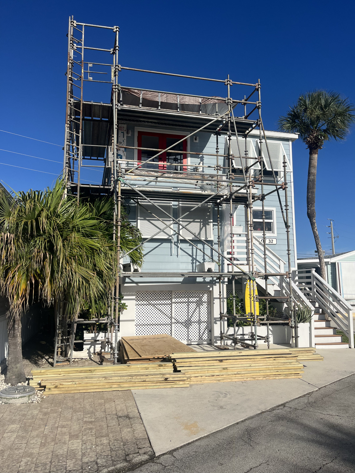 A house undergoing home renovation stands amidst palm trees, with scaffolding set up by a skilled general contractor.