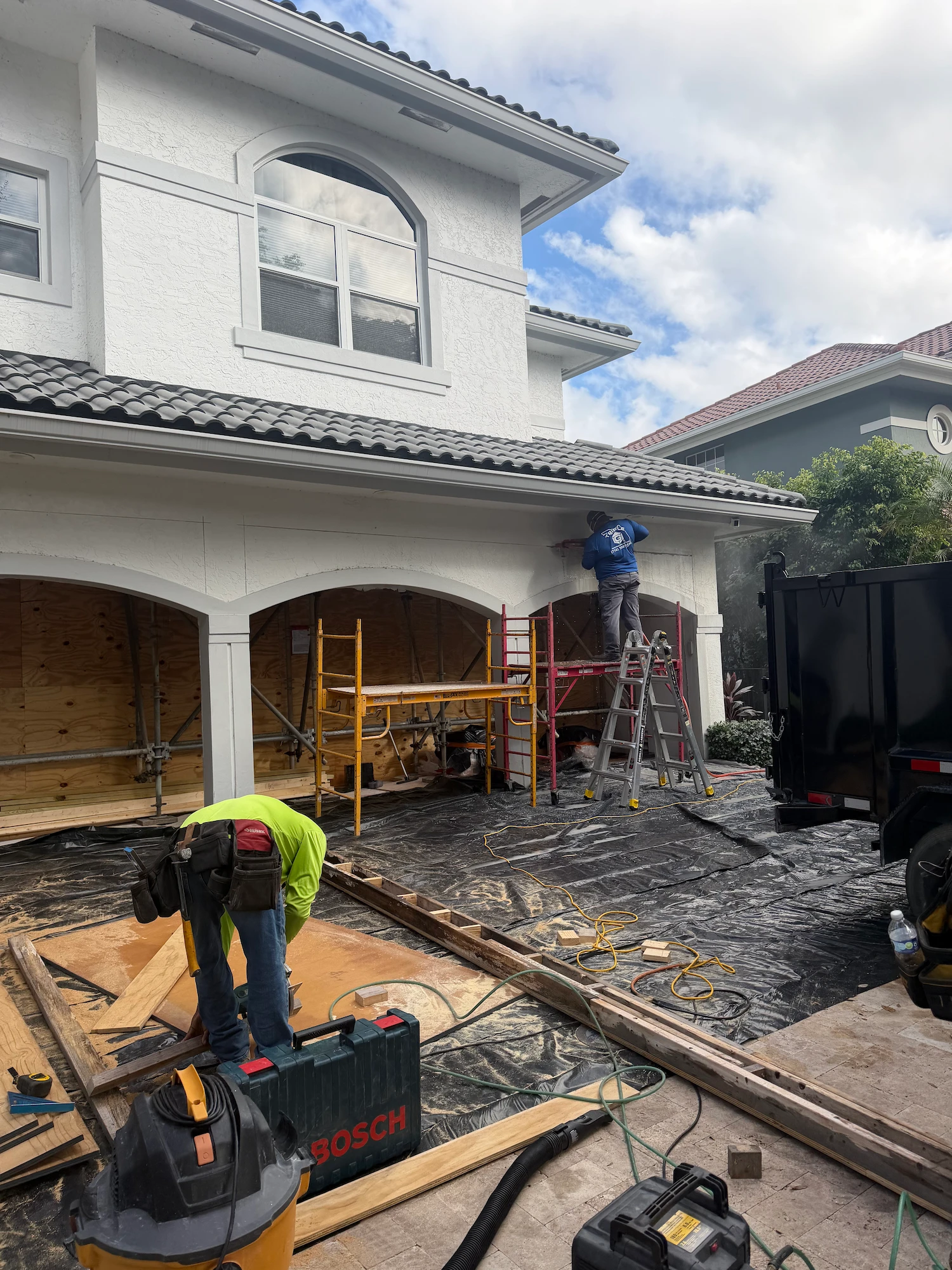 Residential exterior renovation in progress by Nakamura Contractors Corp — two-story South Florida home with scaffolding and crew working on facade and garage remodel